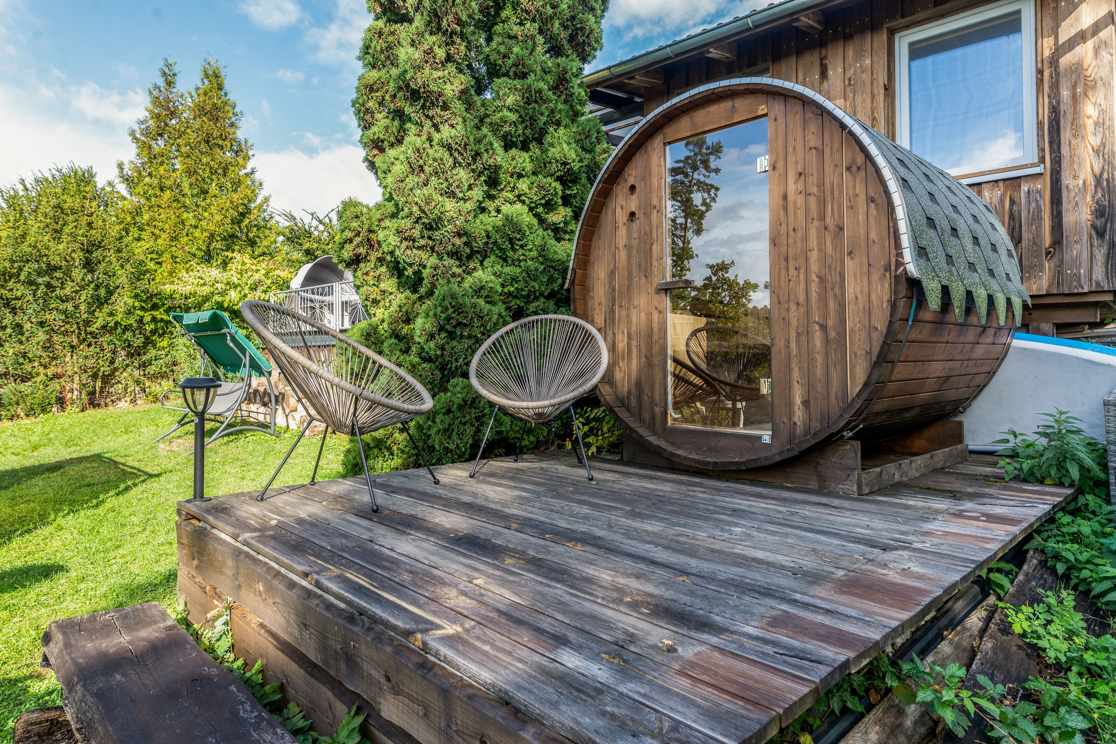 Eine Holzbütte mit Fenster, umgeben von einer Holzterrasse und zwei Korbstühlen.