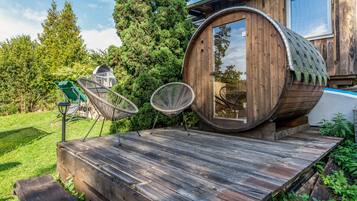 Eine Holzbütte mit Fenster, umgeben von einer Holzterrasse und zwei Korbstühlen.
