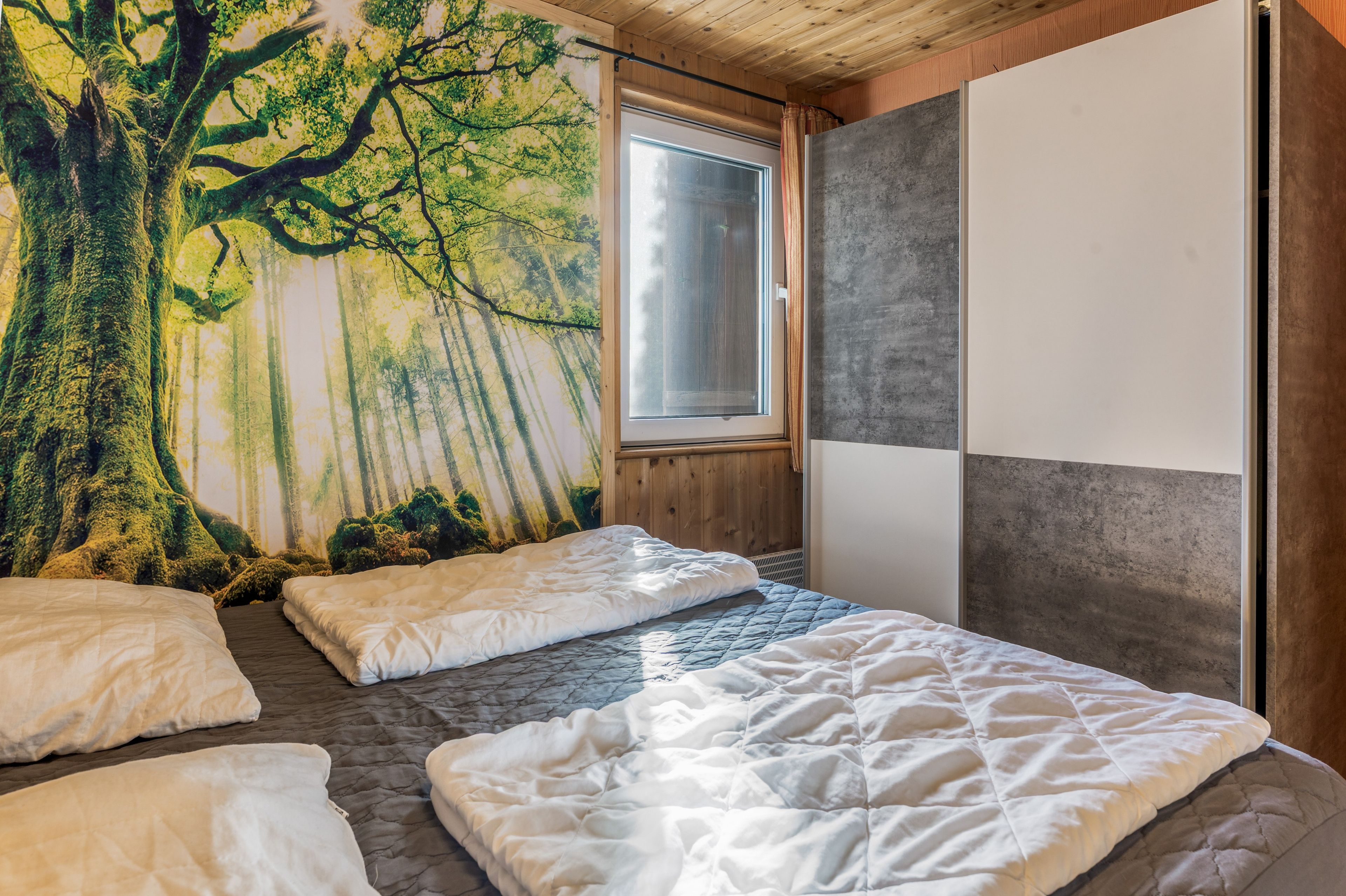 Ein Schlafzimmer mit einer großen Waldmalerei, einem Fenster und einem Bett mit vielen Kissen.