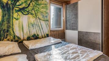 Ein Schlafzimmer mit einer großen Waldmalerei, einem Fenster und einem Bett mit vielen Kissen.