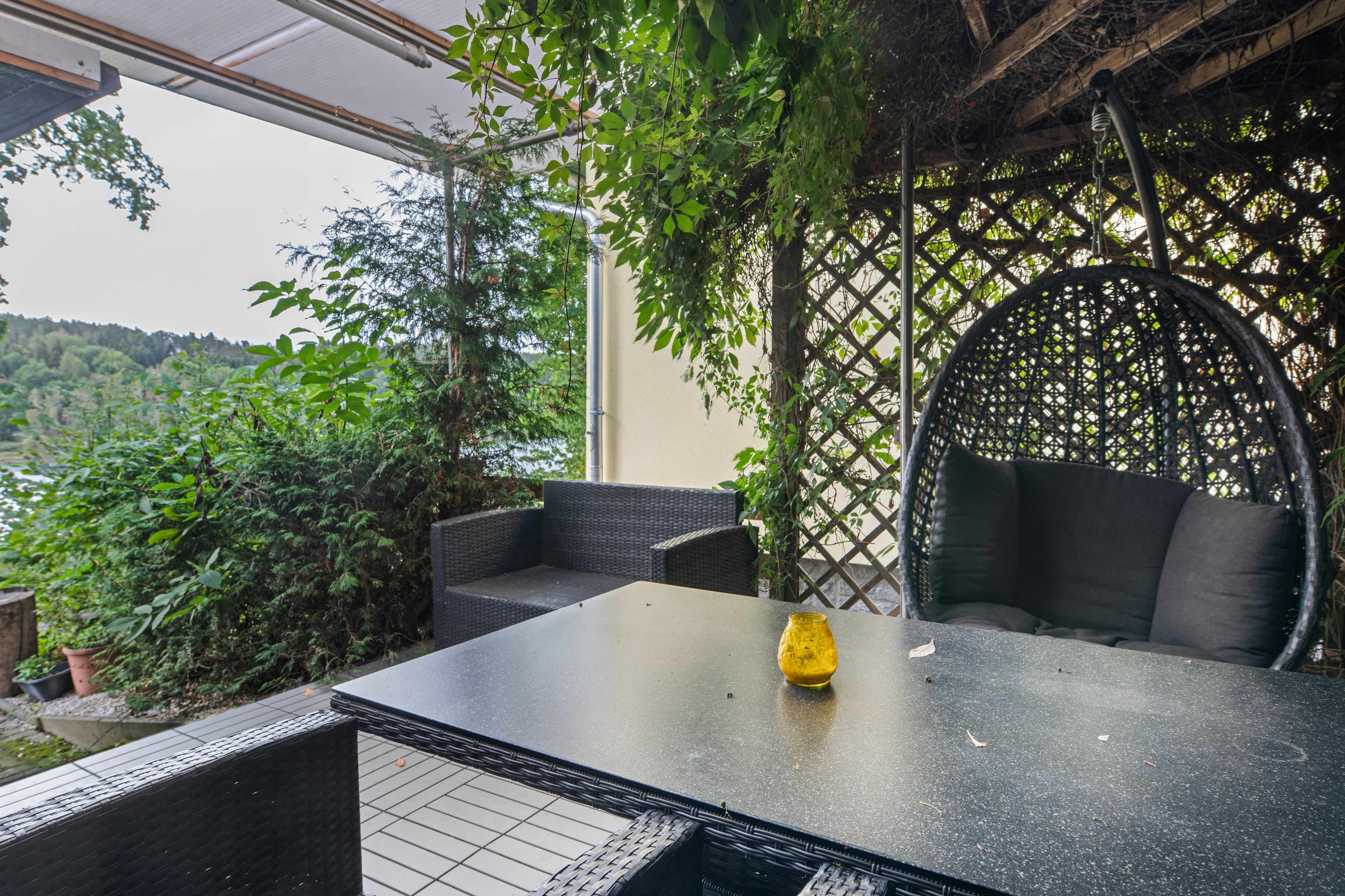 An outdoor seating area with a table and chairs, surrounded by greenery and a view of the landscape.
