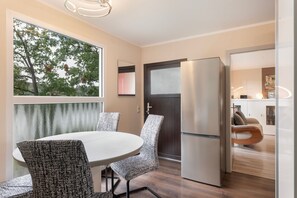 A modern kitchen with a built-in refrigerator, a dining area with patterned chairs, and a large window with a view of trees.