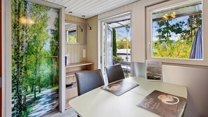 Una habitación con una mesa de comedor, sillas, una estantería, un espejo y una ventana con vistas a árboles.