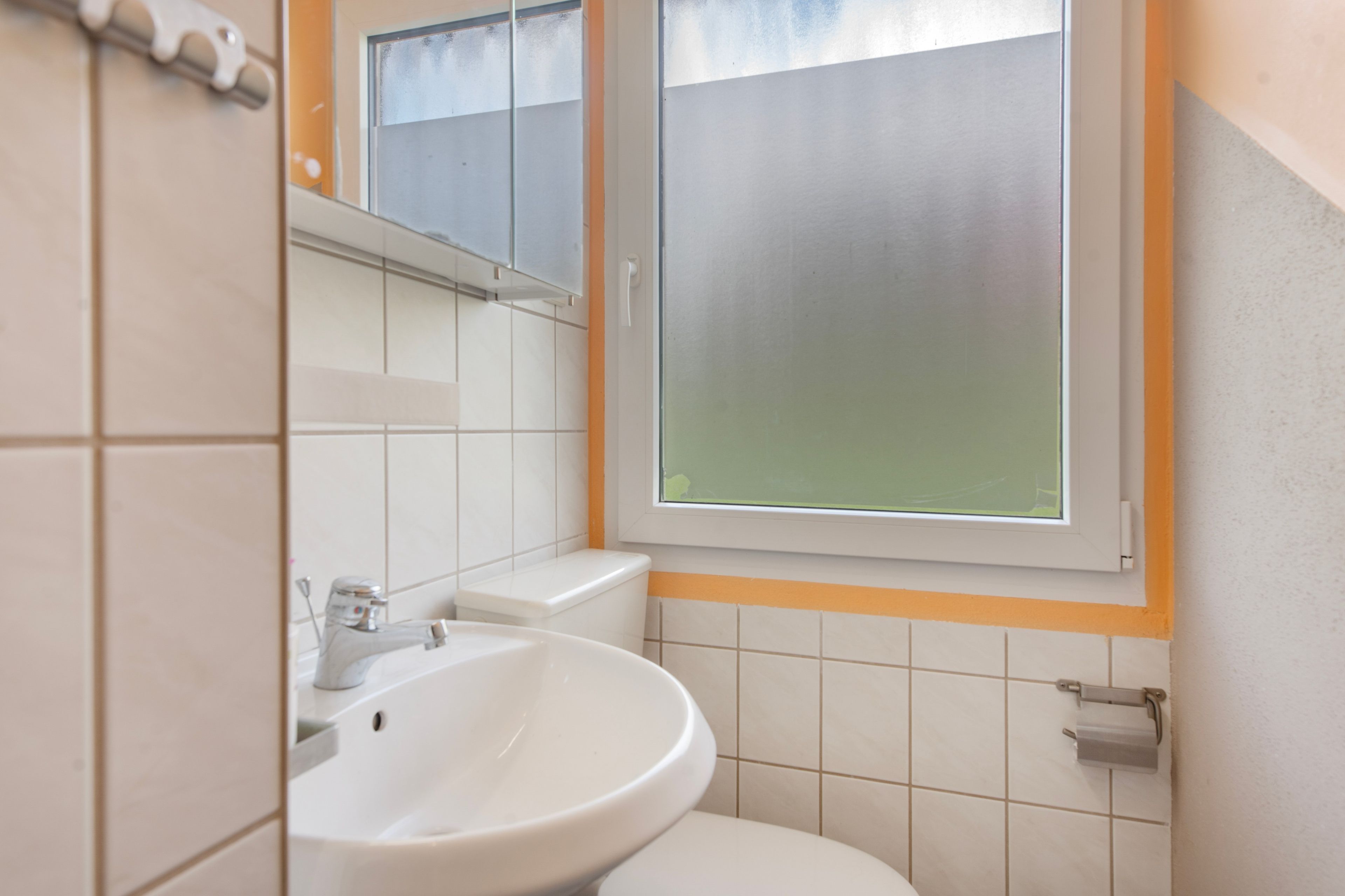 Un bagno con un lavandino bianco, un WC e una finestra con vetro satinato.