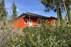 A red building with a balcony and a window, surrounded by greenery.