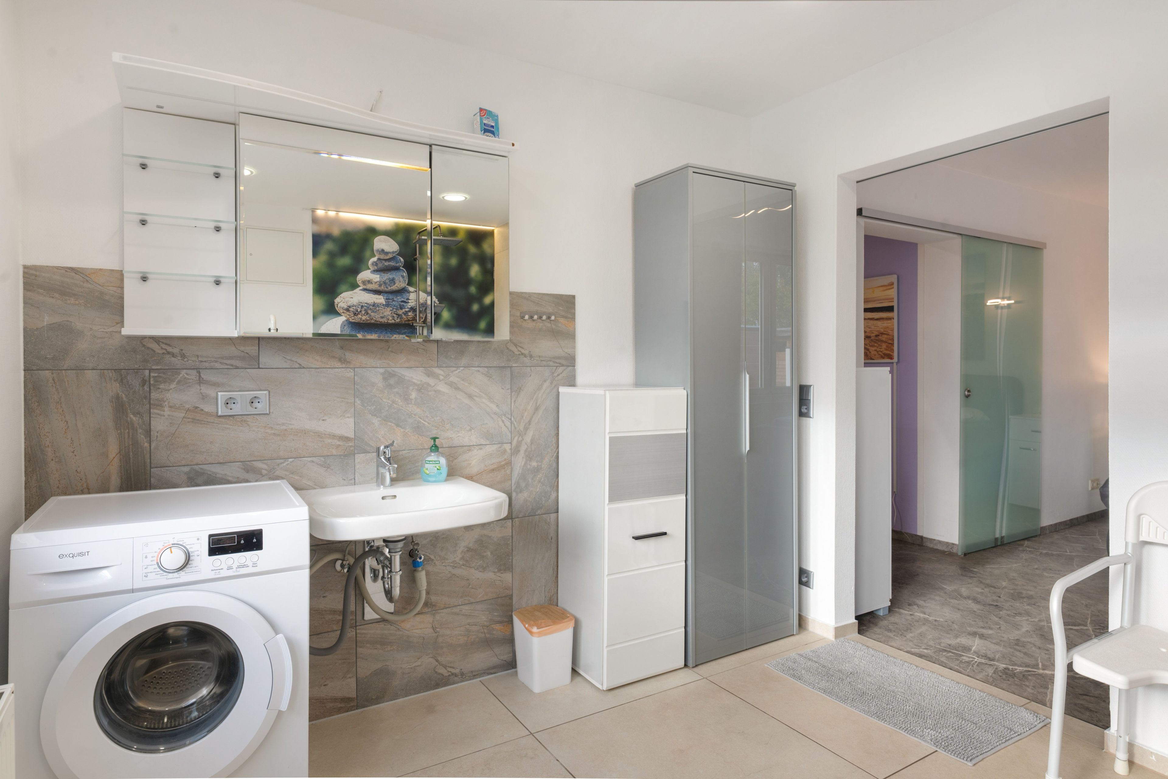 Une salle de bain moderne équipée d’un lave-linge intégré, d’un évier et d’un meuble de rangement.
