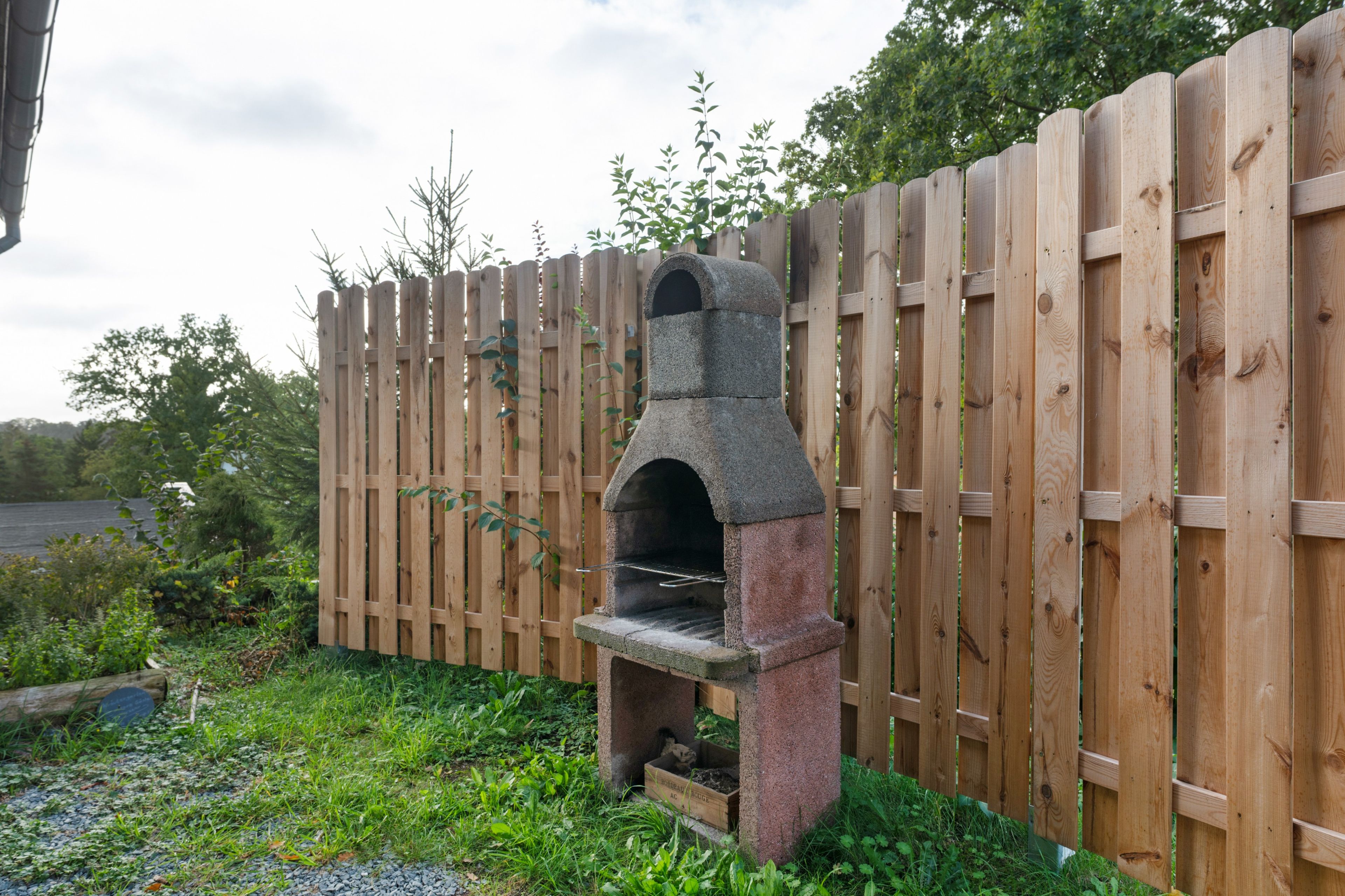 A stone-built outdoor oven with a wooden fence in the background.