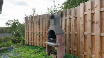 A stone-built outdoor oven with a wooden fence in the background.