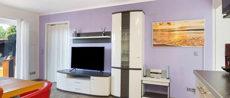 A modern living room with a flat-screen TV, a glass cabinet, and a painting on the wall.