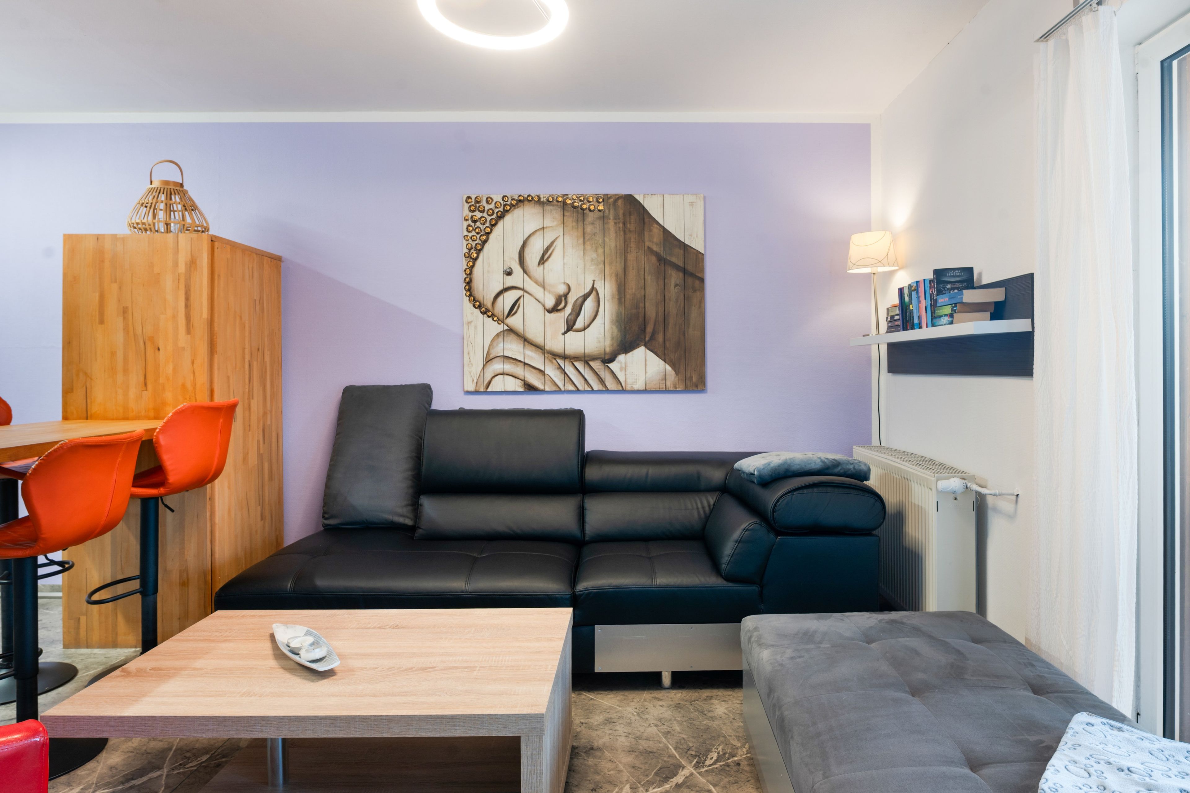 Ein modernes Wohnzimmer mit einem schwarzen Ledersofa, einem Holzesstisch mit orangefarbenen Stühlen, einem Couchtisch und einer Wandleuchte.