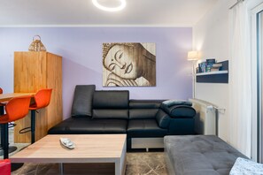 Una sala de estar moderna con un sofá de cuero negro, una mesa de comedor de madera con sillas naranja, una mesa de centro y una lámpara de pared.
