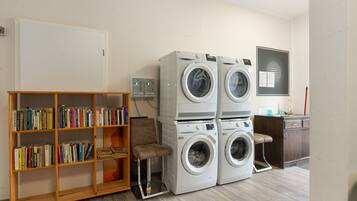 A laundry room with stacked front-loading washing machines, a wooden bookshelf with books, and a desk with a computer.