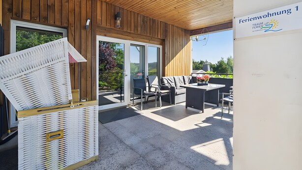 Un área de estar al aire libre techada, con techo de madera, puerta de vidrio que da al exterior y un cartel que indica 'Ferienwohnung 1'.