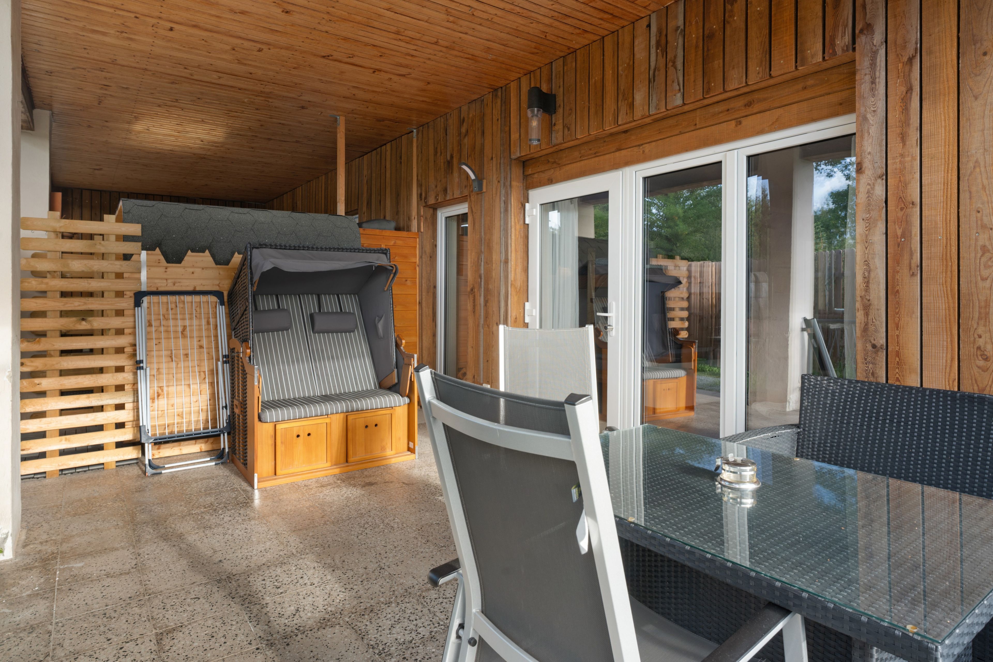 Una cabaña de madera con una mesa y sillas de vidrio, una cama litera y un gran ventanal que da al exterior.