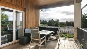 Un espace extérieur abrité, doté d’une table et de chaises, d’une porte-fenêtre coulissante et offrant une vue sur les arbres et le ciel.