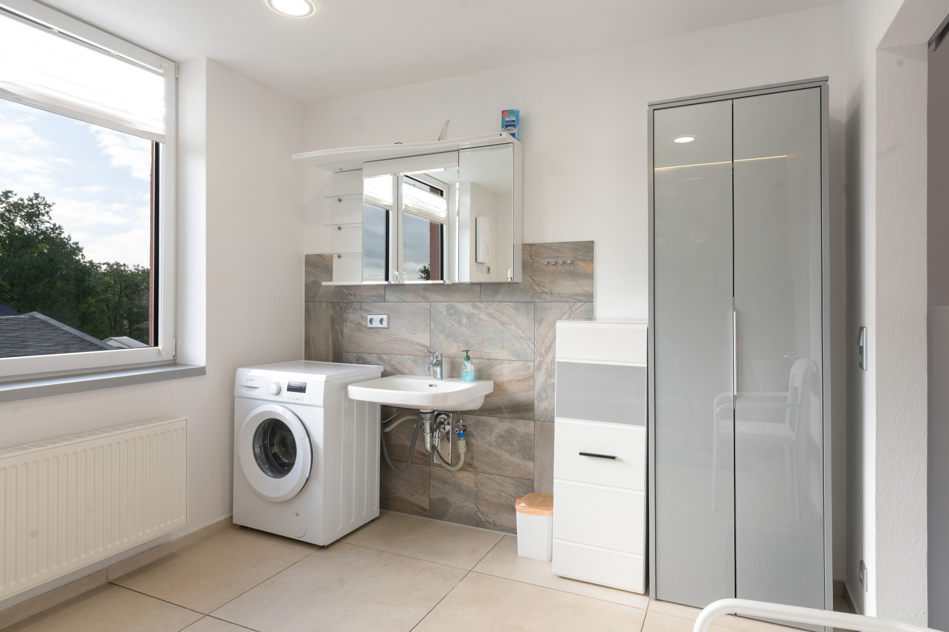 Un baño moderno con lavadora, lavamanos y zona de ducha.