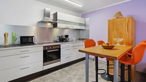 Una cocina moderna con armarios blancos, microondas, horno y comedor con mesa de madera y sillas naranjas.