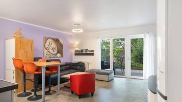 A modern living space with a dining area, a sofa, a red ottoman, a wooden cabinet, and a painting on the wall.