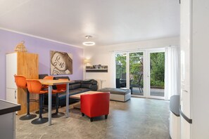A modern living space with a dining area, a sofa, a red ottoman, a wooden cabinet, and a painting on the wall. - Apartment “Zum Segel” 1 with Private Terrace and Wi-Fi (Zadelsdorf)