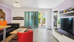 Una sala de estar moderna con un sofá, una butaca roja, una mesa de centro, un televisor y una estantería.