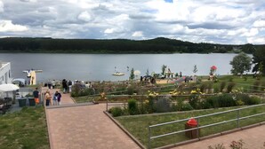 Vista sobre un lago con un camino pavimentado, zonas verdes y un muelle con barcos.