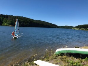 Una persona practica windsurf en un lago tranquilo con una orilla arbolada.