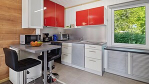 Une cuisine compacte avec des meubles blancs et rouges, un four à micro-ondes, un grille-pain et une fenêtre donnant sur un paysage verdoyant.
