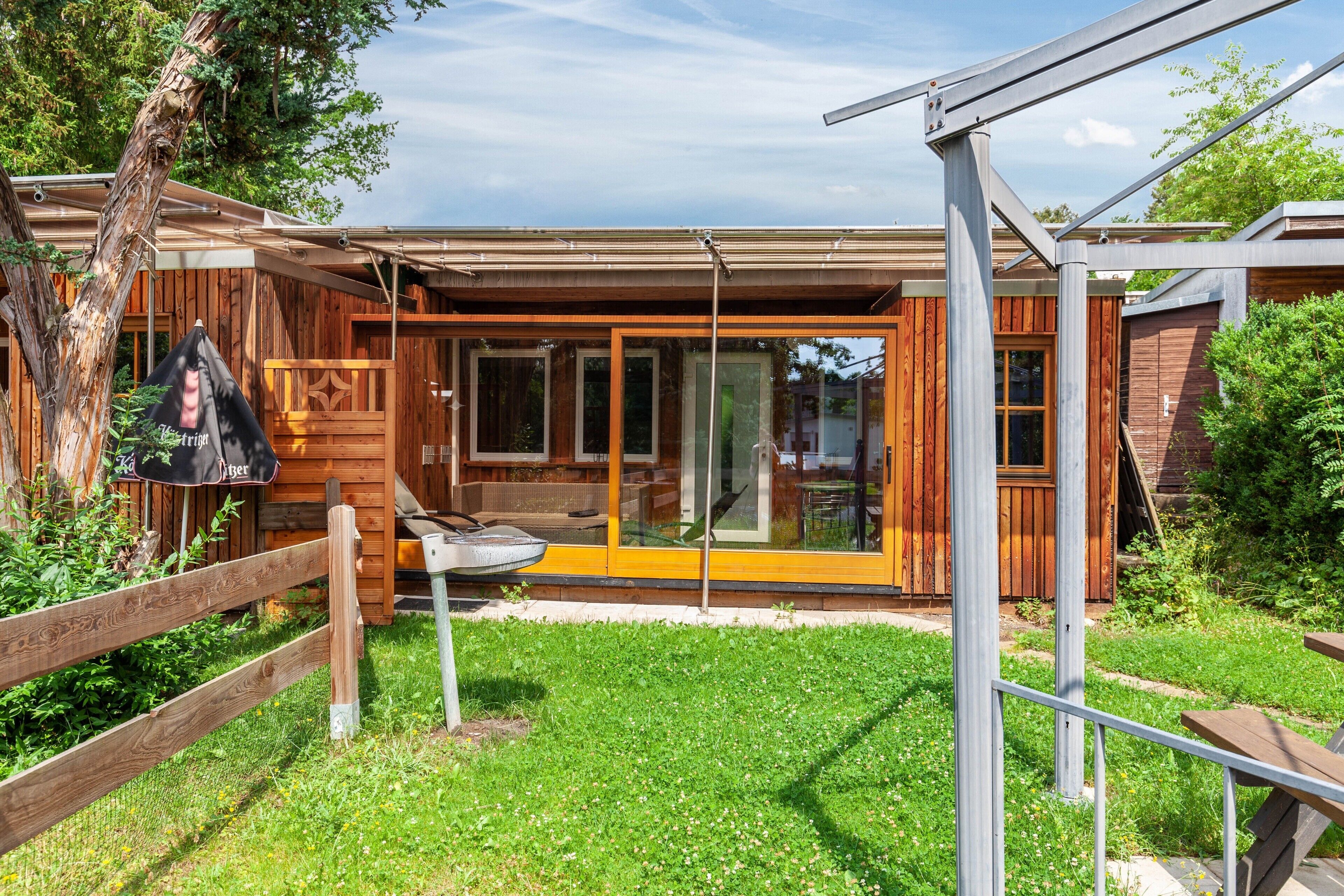 A modern house with a glass-enclosed porch, wooden deck, and a metal railing.