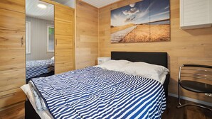 Une chambre avec une armoire à miroir, un lit avec une literie à rayures, un tableau représentant un paysage et une chaise.