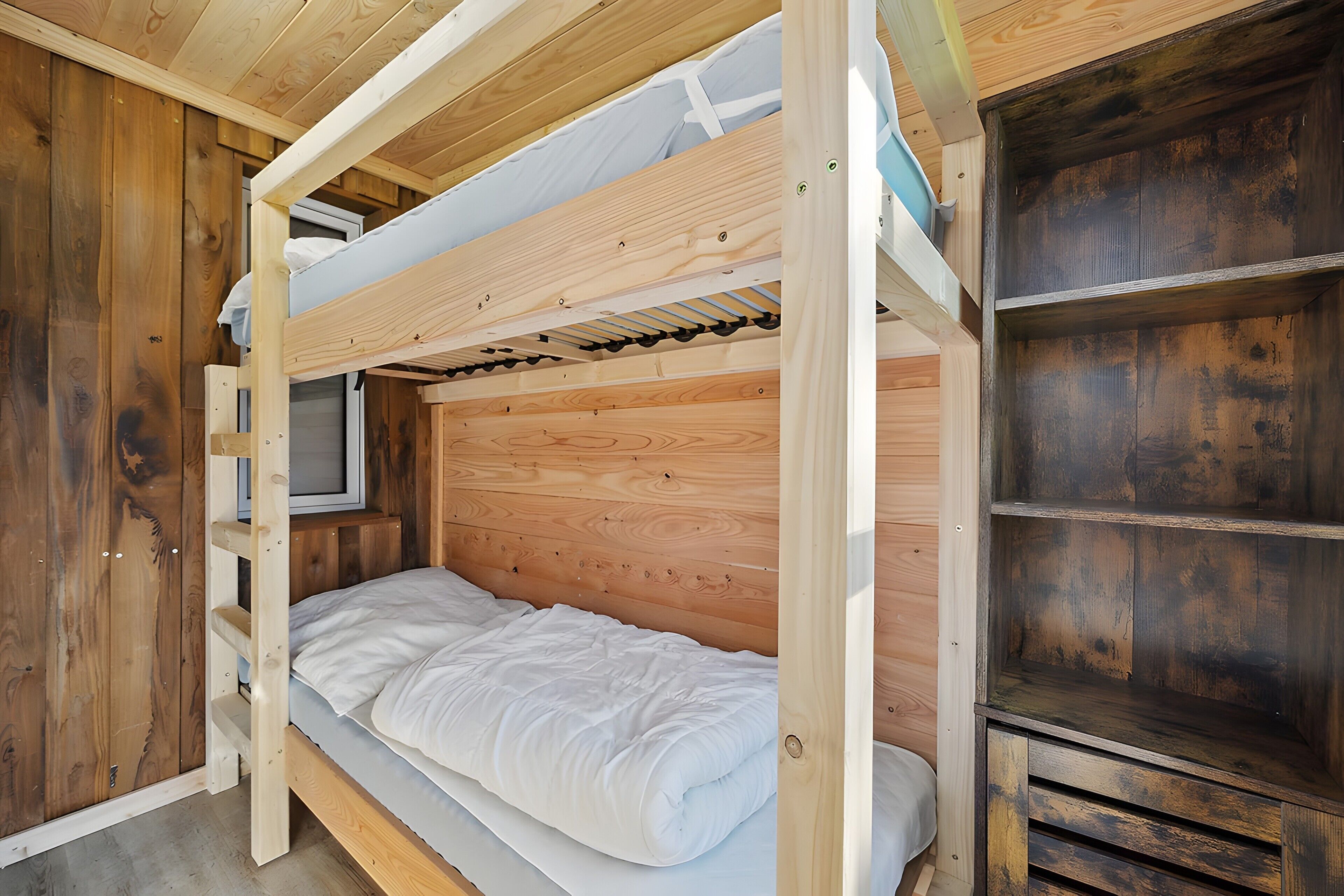 Habitación con literas, paredes de madera, un televisor y una estantería.