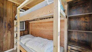 Habitación con literas, paredes de madera, un televisor y una estantería.