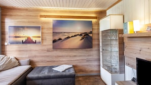 Een kamer met houten paneelwanden, een bank, een met kussens beklede zitting, een glazen kast met glazen en twee ingelijste foto's.