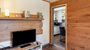 Een moderne kamer met een houten wand, een flatscreen televisie, een plank met elektronische apparaten en een doorgang naar een keuken.