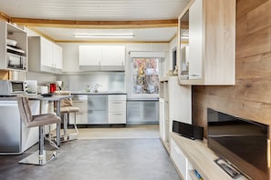 A modern kitchen with white cabinets, a dining area with bar stools, a built-in TV, and a window with a view.