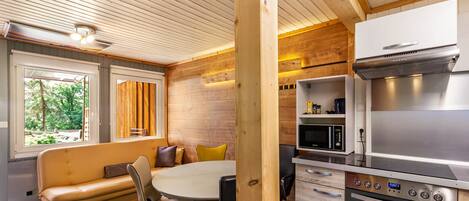 Een moderne keuken met een ingebouwde oven en magnetron, een houten plafond en een eethoek met een bank en stoelen.