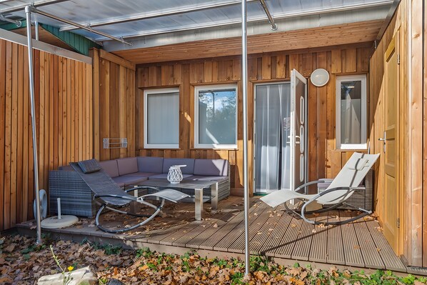 A wooden cabin with a patio area, including a sofa, chairs, and a table.