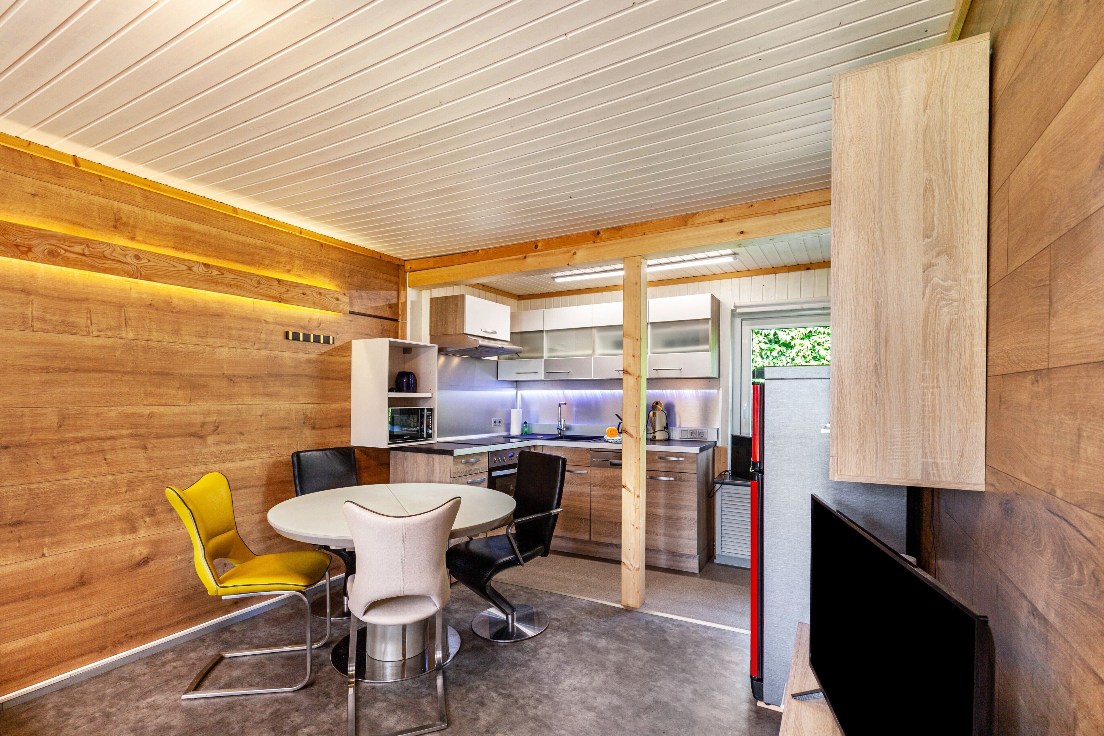 Una cocina moderna con paredes de madera, un comedor con sillas amarillas y un televisor.