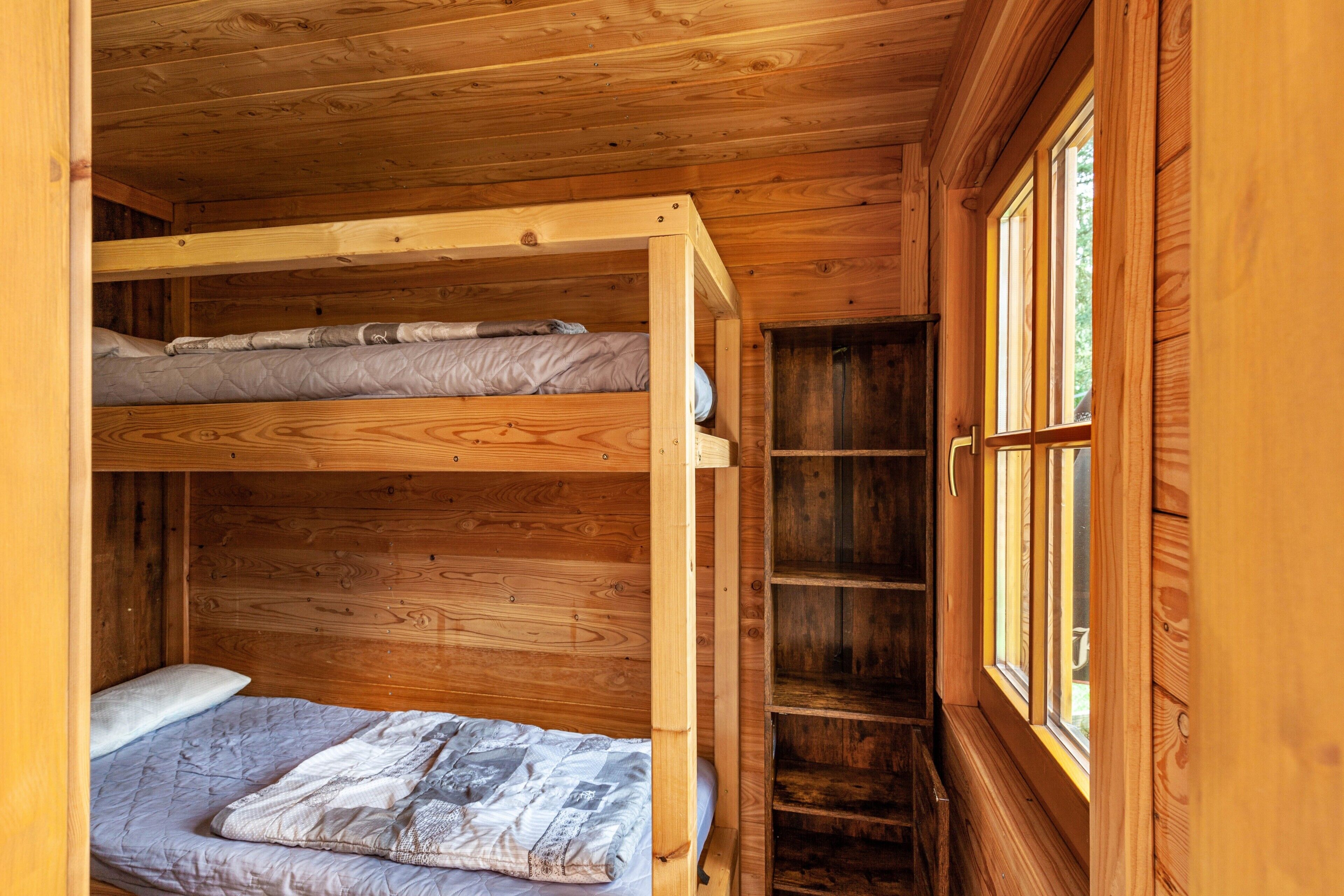 Une chambre avec un lit superposé en bois, une fenêtre et des étagères intégrées.