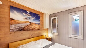 Een slaapkamer met een houten hoofdeinde, een groot landschapsschilderij, een bedlampje en een raam met uitzicht.