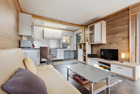 A modern living room with a sofa, coffee table, TV, and kitchen area.