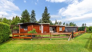 A wooden cabin with a covered porch, a fenced yard, and surrounding trees.