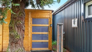 A wooden door with a glass panel, a metal gate, and a tree beside a building.