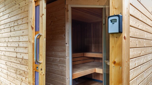 A wooden sauna with a door open, revealing a bench inside.