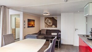 A modern room with a dining table, a sofa, a kitchen area, and a painting on the wall.