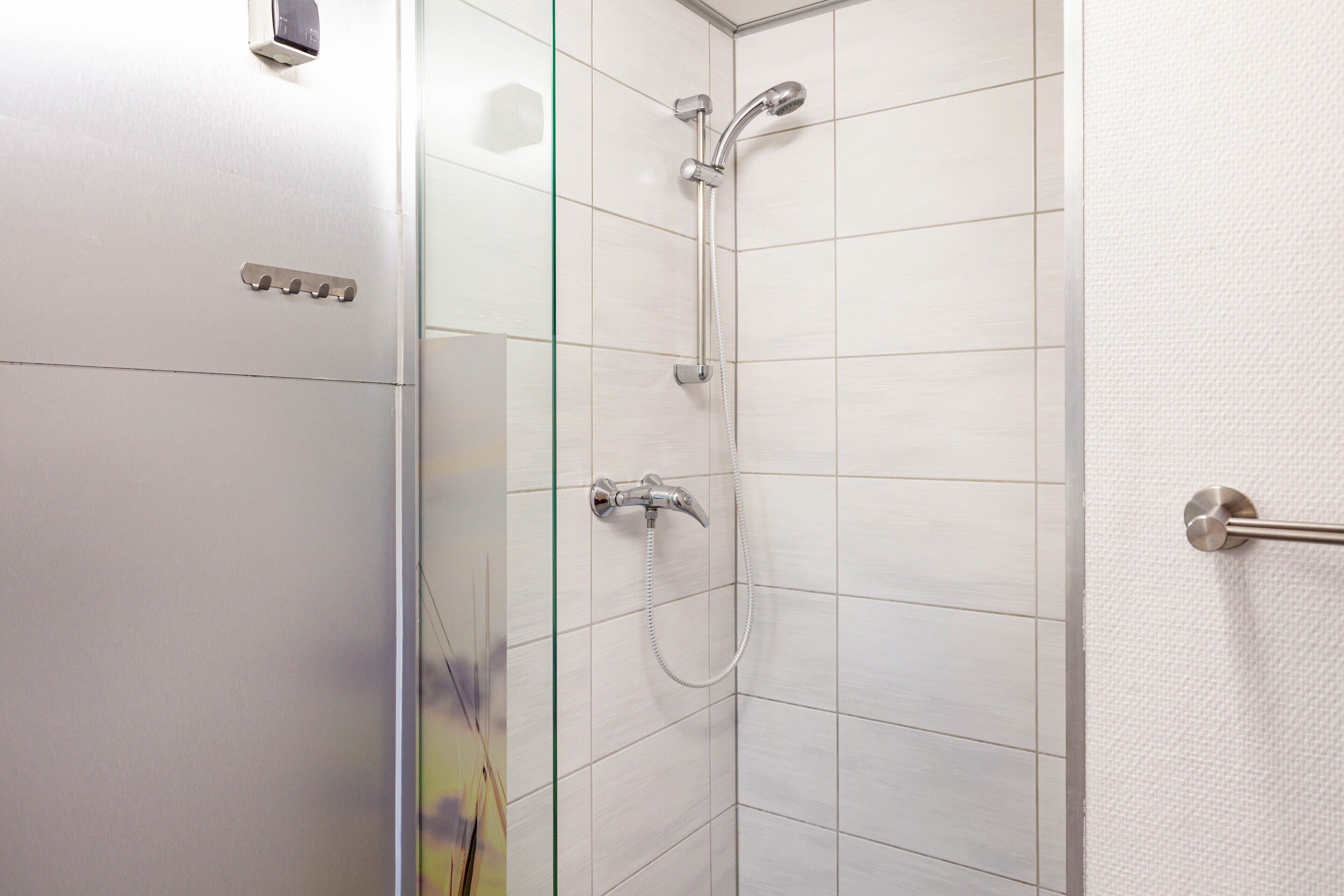 Une douche équipée d’un pommeau de douche à main et d’un robinet mural, ainsi que d’un porte-serviettes et d’une paroi en verre.