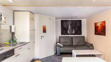 A compact living space with a kitchenette, a gray sofa, a white table, and artwork on the walls.