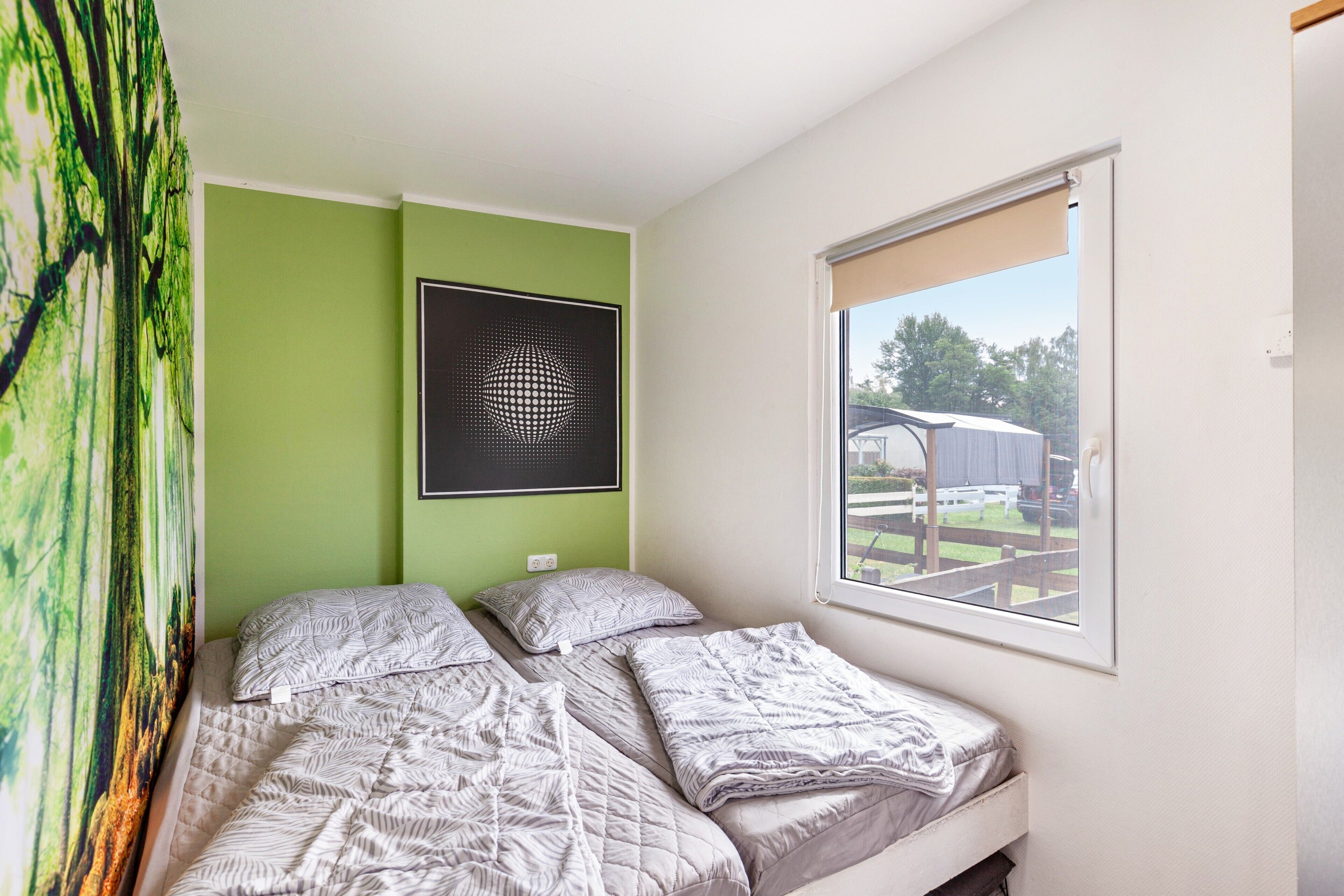 A bedroom with a bed, a window, a green wall, and a framed artwork.