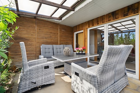 A patio with wicker furniture, a grey sofa, and a table with flowers.. Holiday Home 'Ferienhaus 34' with Private Terrace, Shared Garden and Wi-Fi