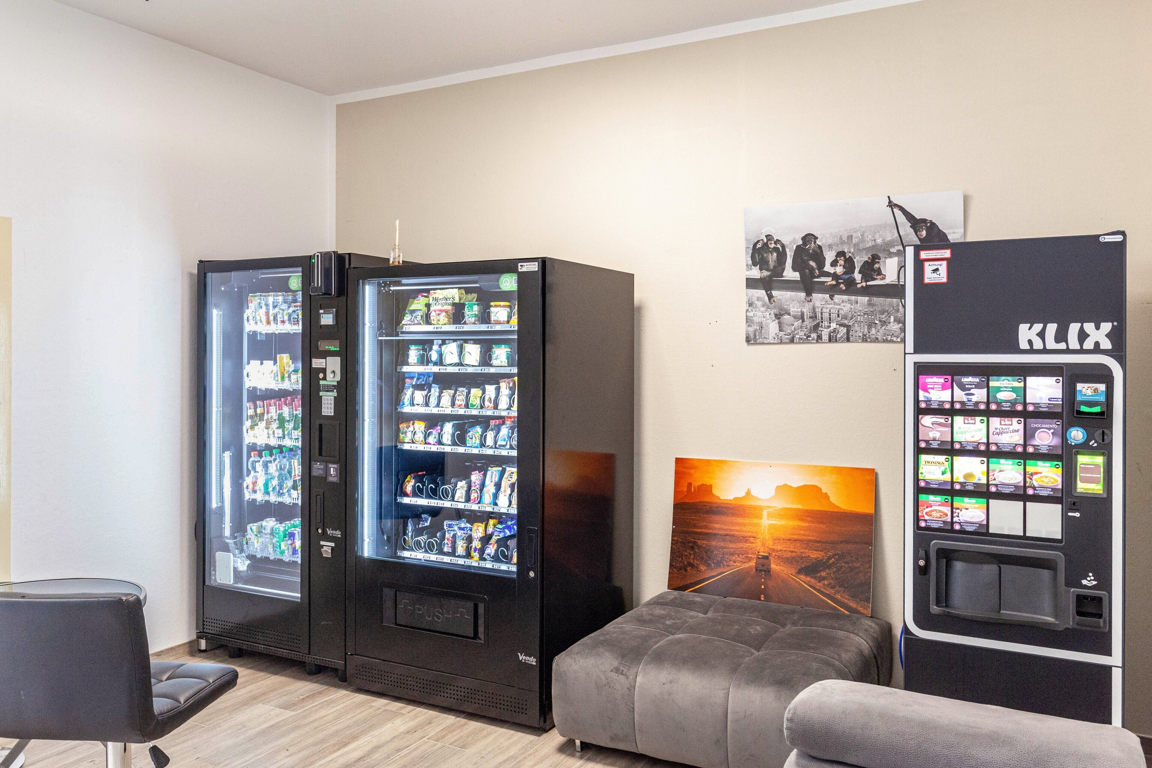 Une pièce équipée de deux distributeurs automatiques de boissons, d’un canapé gris et d’un tableau accroché au mur.