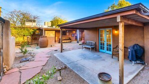 A patio area with a barbecue grill, a wooden bench, and a large planter.